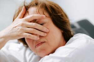 A woman is leaning forward with her hand over her face and her eyes closed
