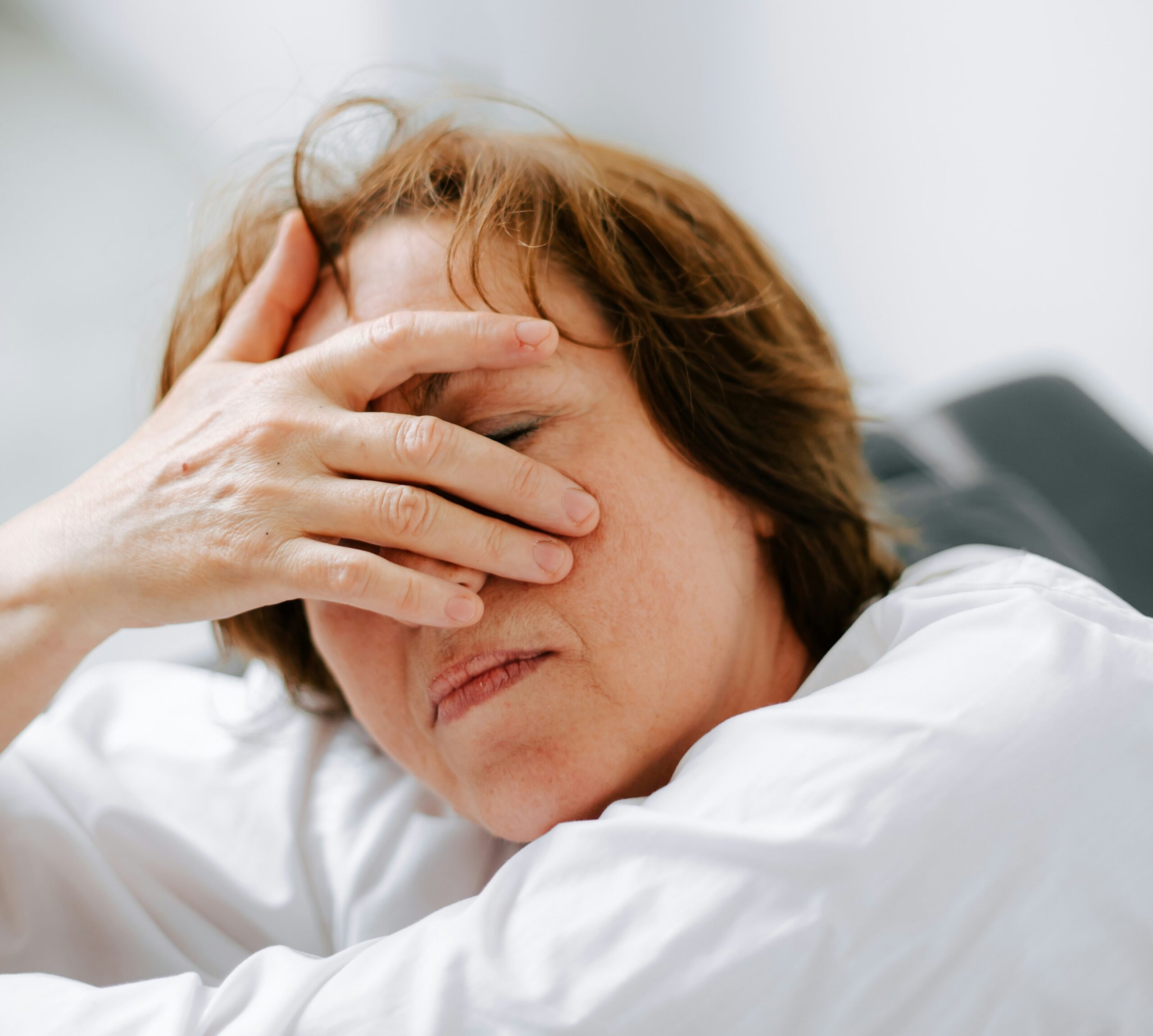 A woman is leaning forward with her hand over her face and her eyes closed